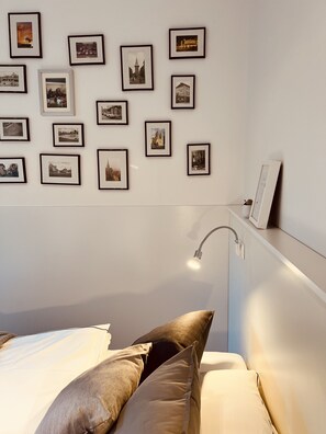 A bedroom with a bed, pillows, a bedside table, a lamp, and a wall with framed pictures. - Charming rear building near the old town (Osnabrück)