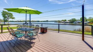 Een terras met buitenmeubilair, een groene parasol en uitzicht op een meer.