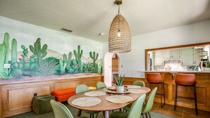 Een eethoek met een ronde tafel, groene stoelen, een cactusmuur en een hanglamp.