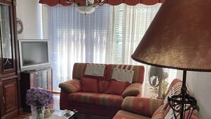A living room with a sofa, a glass coffee table, a TV, and a lamp. - Apartamento Playa Ladeira (Santa Cristina da Ramallosa)