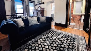 Ein Wohnzimmer mit einem dunkelblauen Sofa, einem gemusterten Teppich und einer Uhr an der Wand.
