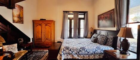 A bedroom with a bed, a wooden wardrobe, a desk, a chair, a lamp, and a window with curtains.