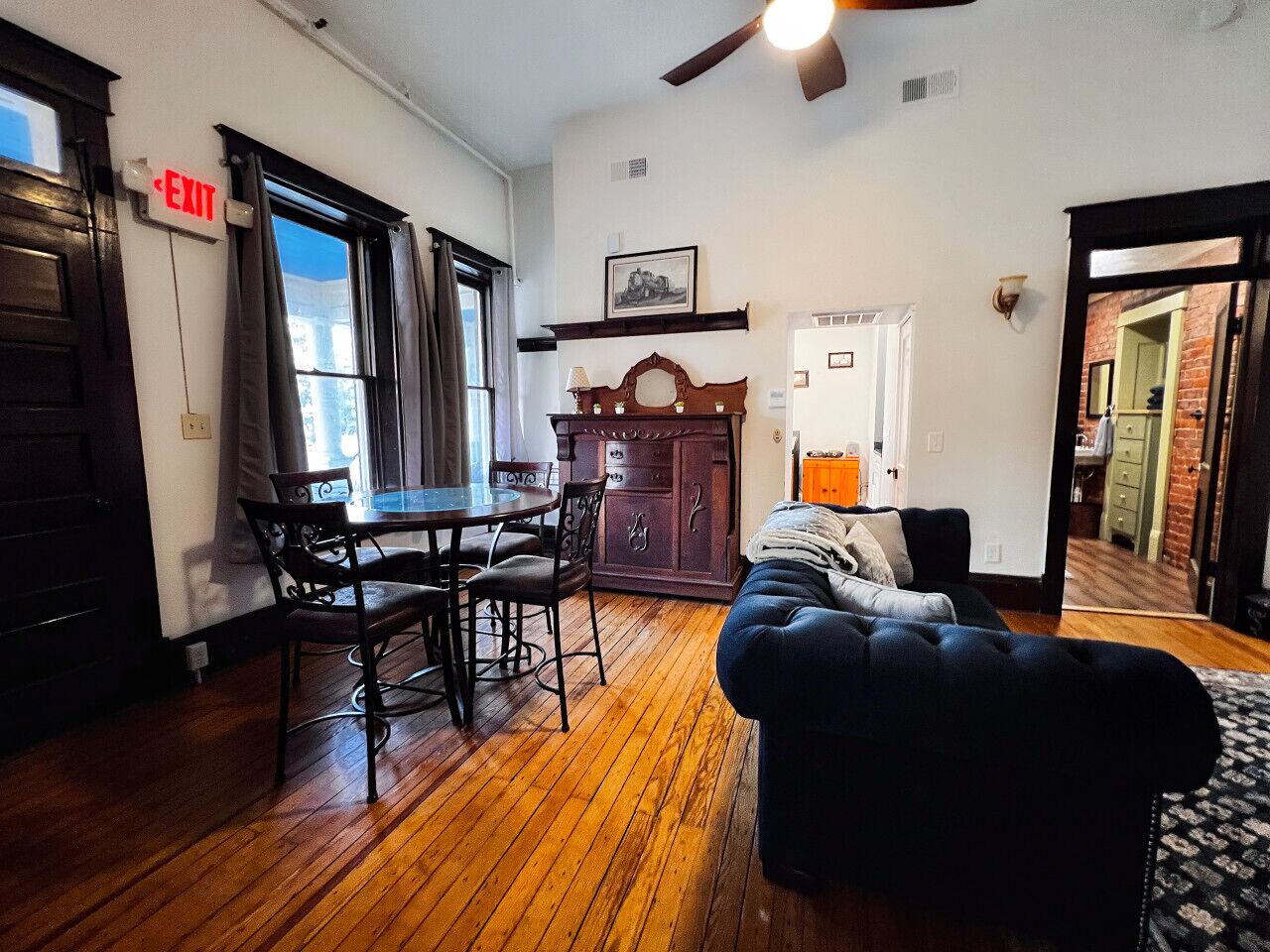 A room with a dining table, chairs, a sofa, and a kitchen area.