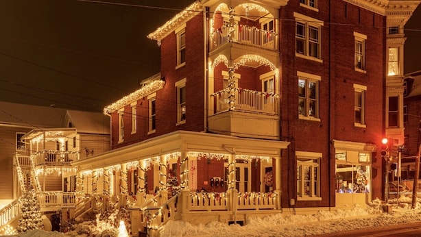 Ein zweistöckiges Backsteinhaus mit Balkon und einer mit Lichtern und Weihnachtsbäumen geschmückten Veranda.