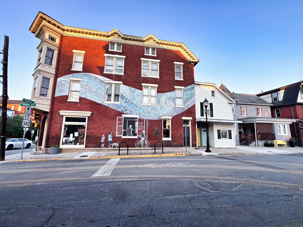 A red brick building with a large mural on the side, located at an intersection with a crosswalk and traffic lights.