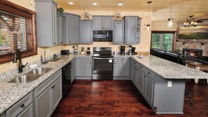 A modern kitchen with grey cabinets, stainless steel appliances, granite countertops, and a built-in island. - Quittin Time - Hot Tub, Game Room & Home Theater (Gatlinburg)