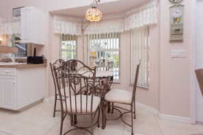 Cozy kitchen area with a round dining table and four cushioned chairs, featuring white cabinetry and a countertop with appliances.