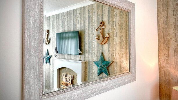 A mirror with a decorative frame, reflecting a room with a television, a decorative anchor, and a star on the wall. - Remarkable 3-bed Hot Tub House in Blackpool (Blackpool)