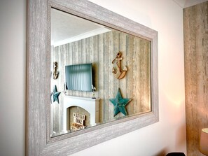 A mirror with a decorative frame, reflecting a room with a television, a decorative anchor, and a star on the wall. - Remarkable 3-bed Hot Tub House in Blackpool (Blackpool)