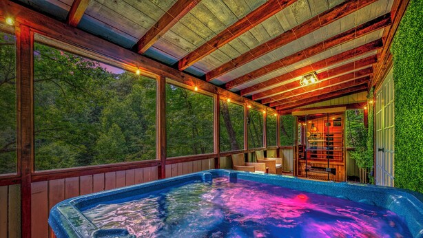 A hot tub with a view of a forest, wooden beams, and a glass door leading to a room. - Zen Zone Spa Cabin! Hot Tub & Sauna! King Beds (Sevierville)
