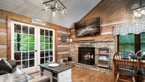 A cozy interior with a stone fireplace, wooden walls, and a 'Welcome' sign. - Zen Zone Spa Cabin! Hot Tub & Sauna! King Beds (Sevierville)