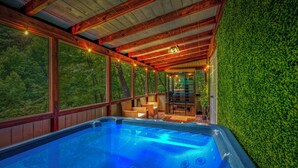 A hot tub area with wooden beams, large windows, and a green wall. - Zen Zone Spa Cabin! Hot Tub & Sauna! King Beds (Sevierville)