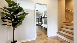 Passadís amb una planta en test, terres de fusta i una escala que porta a una habitació amb lliteres.