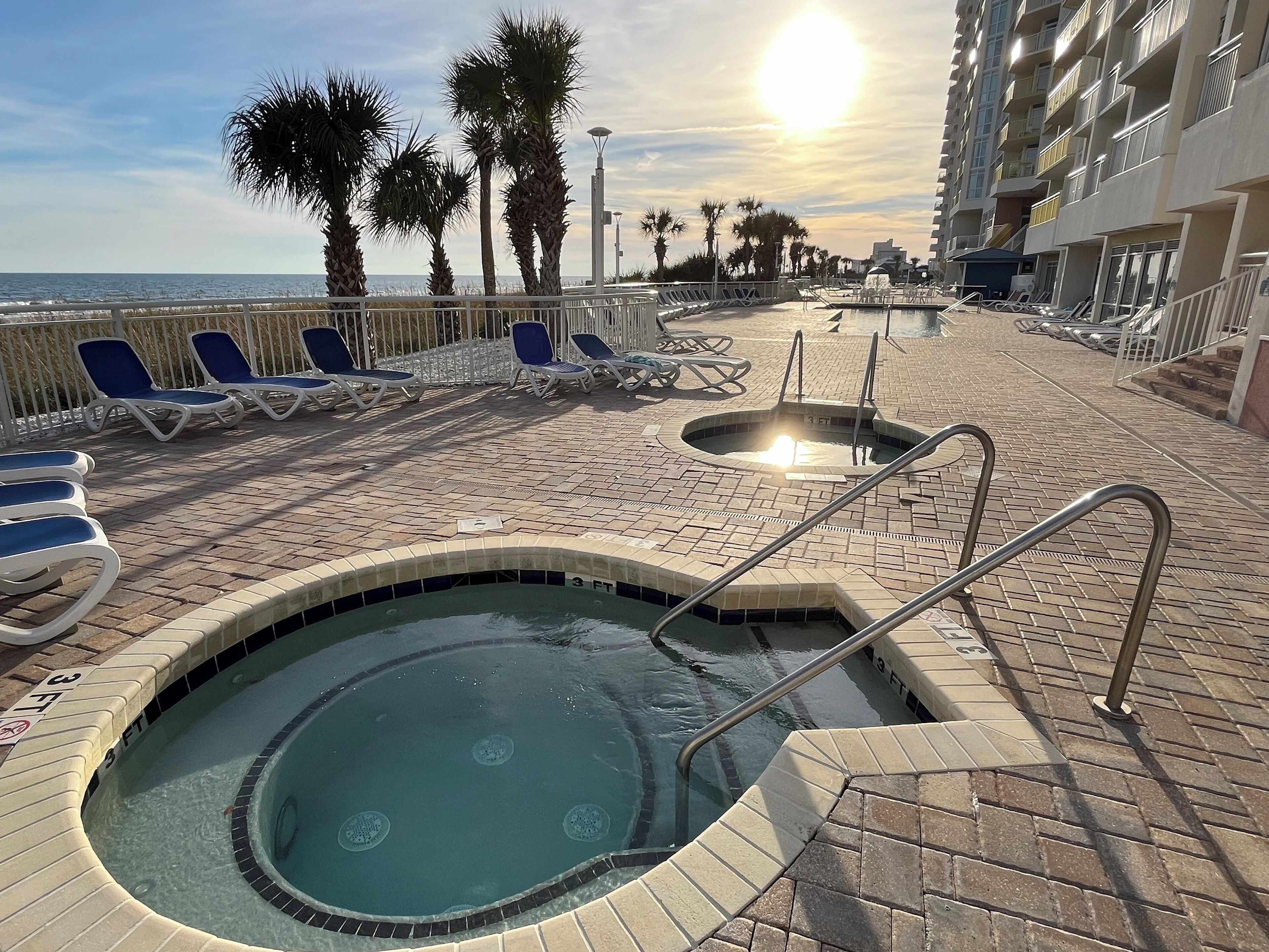 A pool area with lounge chairs, a hot tub, and a view of the ocean.