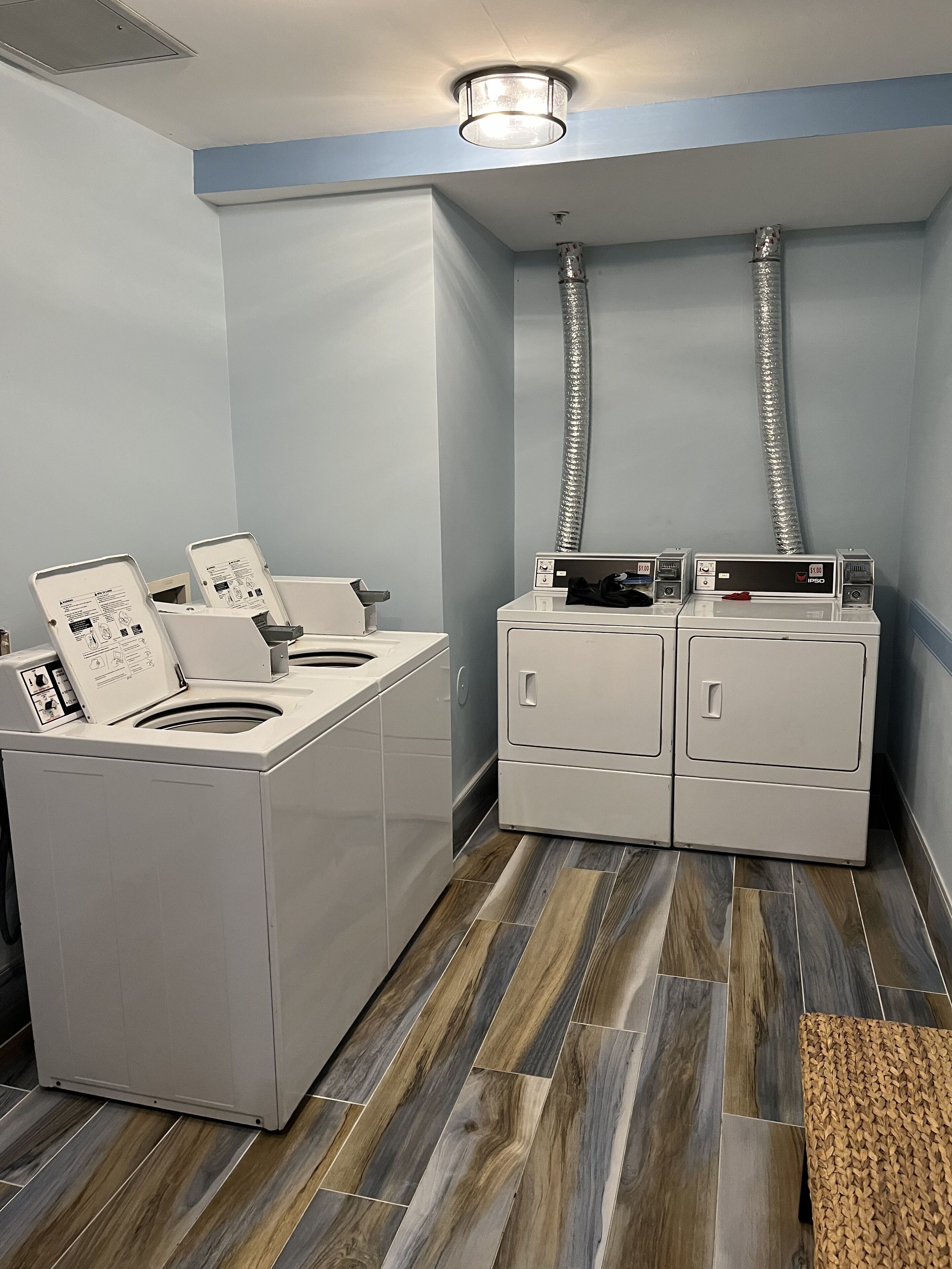 A laundry room with two washing machines and a dryer, a wooden floor, and a blue wall.