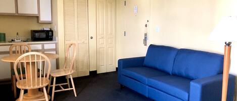 A compact living space with a kitchenette, a blue sofa, and a dining area with wooden chairs.