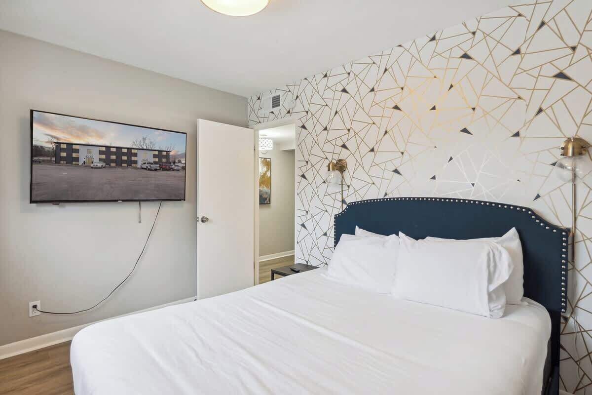 A hotel room with a bed, a wall-mounted TV, and a geometric patterned wall.