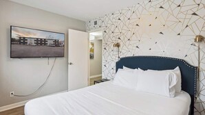 Een hotelkamer met een bed, een aan de muur bevestigde televisie en een wand met een geometrisch patroon.