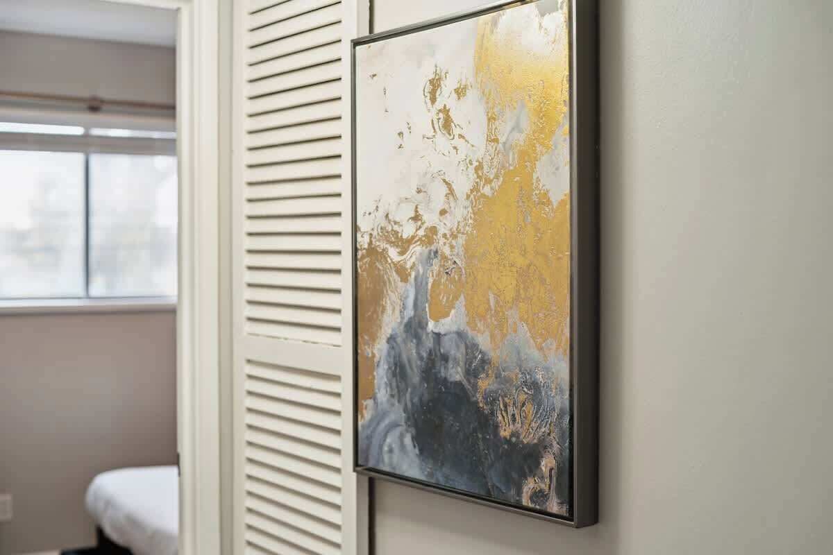 Quarto com cama, janela e pintura abstrata pendurada na parede.