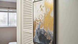 Een kamer met een bed, een raam en een abstract schilderij dat aan de muur hangt.