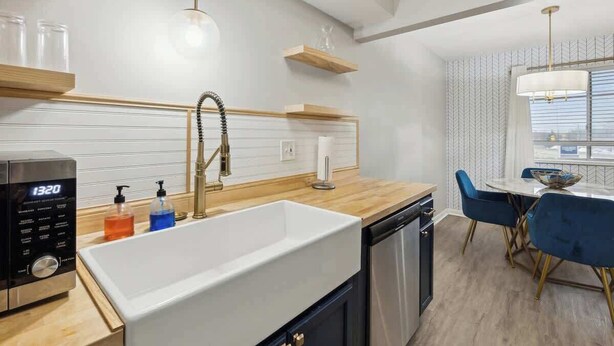 Een moderne keuken met een witte spoelbak, een houten aanrechtblad en een ingebouwde vaatwasser. Er is een eethoek met een ronde tafel en blauwe stoelen.