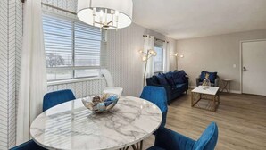 Een moderne woonkamer met een ronde marmeren tafel, blauwe stoelen, een bank en een kroonluchter.