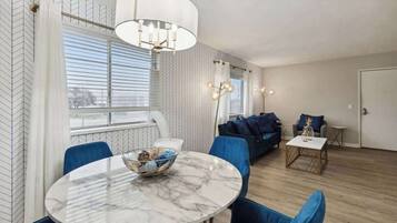 A modern living room with a round marble table, blue chairs, a sofa, and a chandelier.