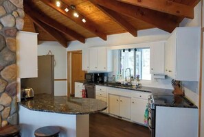 Kitchen with central island, white cabinetry, and stone accent wall, featuring a wooden ceiling with exposed beams and a window.