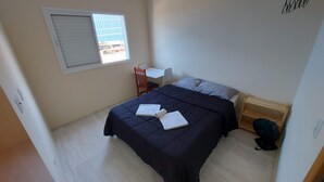 Una camera da letto con un letto, una sedia, un tavolino, una finestra e una mensola in legno.