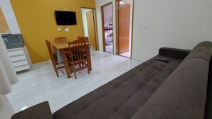 Un soggiorno con un divano marrone, un tavolo da pranzo con sedie, una TV montata a parete e una porta scorrevole che dà su un'altra stanza.