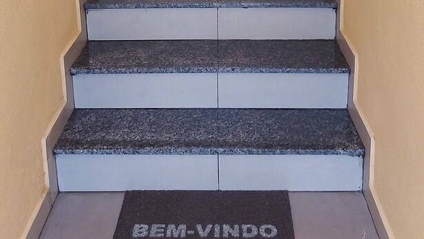 Una scala con ringhiere metalliche, un tappeto con la scritta "Bem-Vindo" e un muro color beige.