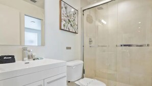 A modern bathroom with a white vanity, a toilet, and a glass-enclosed shower. - Miami Suite 203 (Miami)