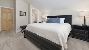 A bedroom with a bed, bedside tables, a nightstand, a wooden door, and a framed picture on the wall.