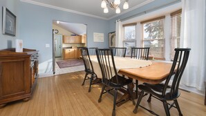 A dining area with a wooden table and chairs, a chandelier, and a view of the kitchen through an open doorway.