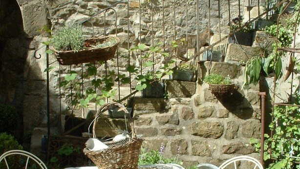 A rustic outdoor seating area with a stone wall backdrop, metal chairs, and a table with a basket. - Château de Rosans (Rosans)