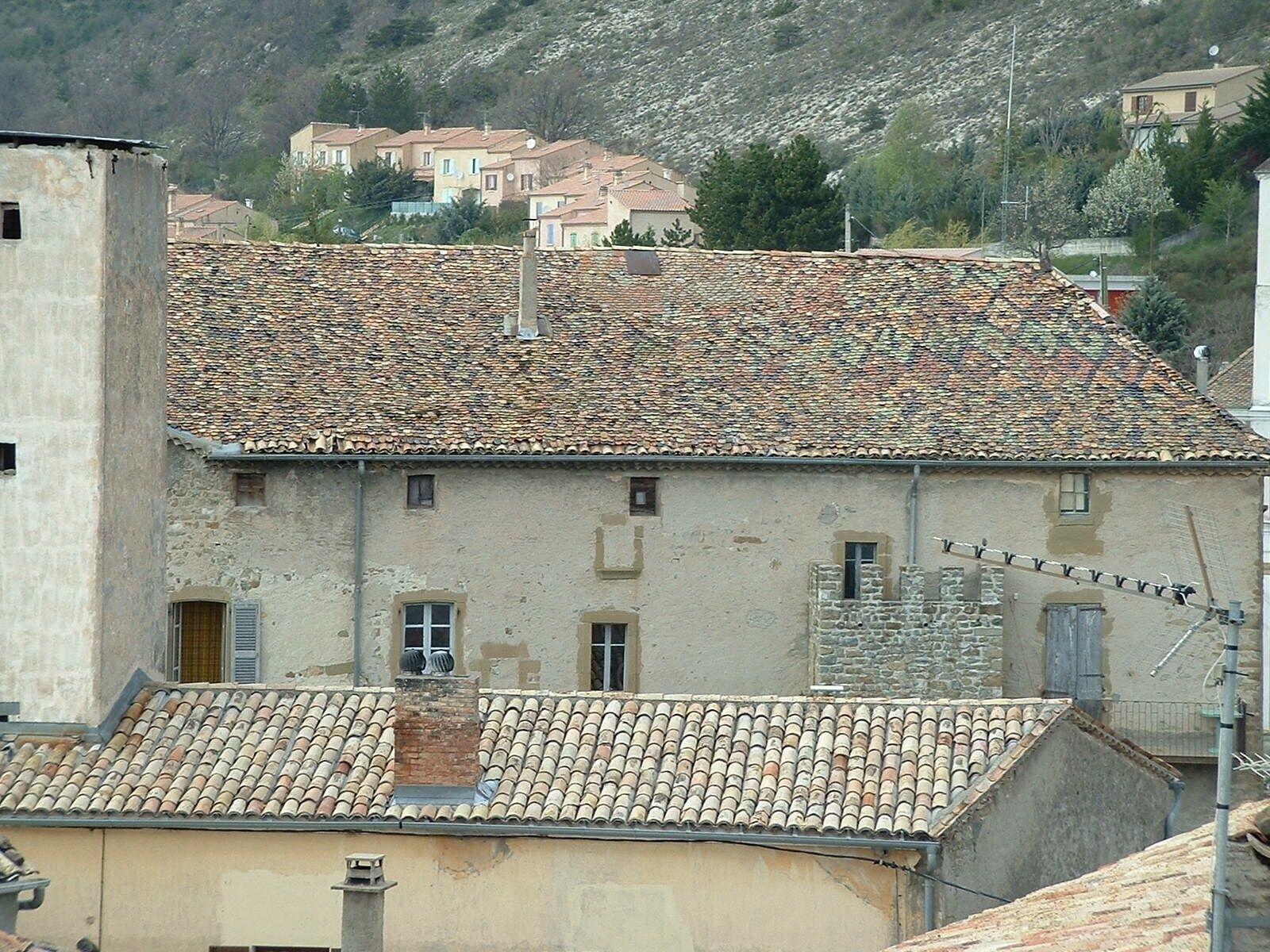 Un bâtiment doté d’un toit en tuiles et de murs en pierre, entouré d’autres bâtiments et situé au pied d’une colline.