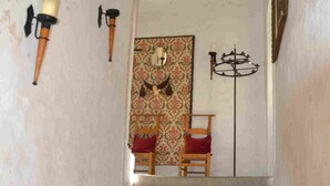 A staircase leading to a room with a patterned tapestry, a wooden chair, and wall-mounted lamps. - Château de Rosans (Rosans)