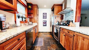 A narrow kitchen with wooden cabinets, a granite countertop, a built-in oven, and a backsplash with a tile pattern.