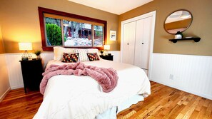 A bedroom with a large bed, a window with a view, a bedside table with a lamp, and a wardrobe.