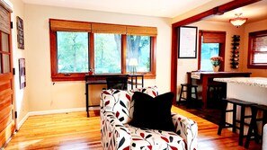 A cozy living room with a patterned sofa, a dining area with a wooden table, and a kitchen with a bar.