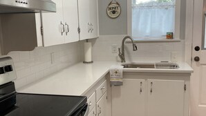 A modern kitchen with white cabinets, a black stove, a window with a view, and a honey-themed wall decoration. - Remodeled Vintage Private Home. <5 min to UF and Downtown (Gainesville)