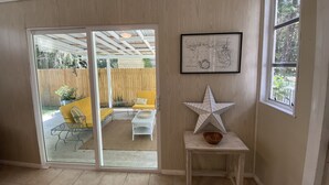 A room with a sliding glass door leading to an outdoor patio area. There is a framed map on the wall, a star-shaped decoration on a small table, and a bowl on the table. - Remodeled Vintage Private Home. <5 min to UF and Downtown (Gainesville)