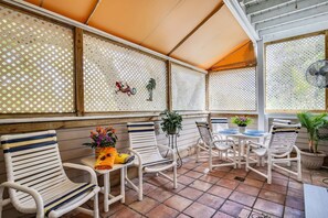 A covered patio area with white wicker chairs and tables, decorative plants, and a fan. - Shared Pool + Gallery Art | Walk to Duval + Southernmost | Duval Sea Turtle (Key West)