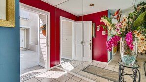 A hallway with red walls, white doors, and a tiled floor. There is a vase with flowers on a small table. - Shared Pool + Gallery Art | Walk to Duval + Southernmost | Duval Sea Turtle (Key West)