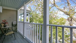 A covered porch with a white railing, a small table with chairs, and a potted plant. - Shared Pool + Gallery Art | Walk to Duval + Southernmost | Duval Sea Turtle (Key West)