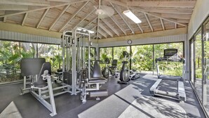 Een overdekte gymzaal met trainingsapparatuur, grote ramen en een plafondventilator.