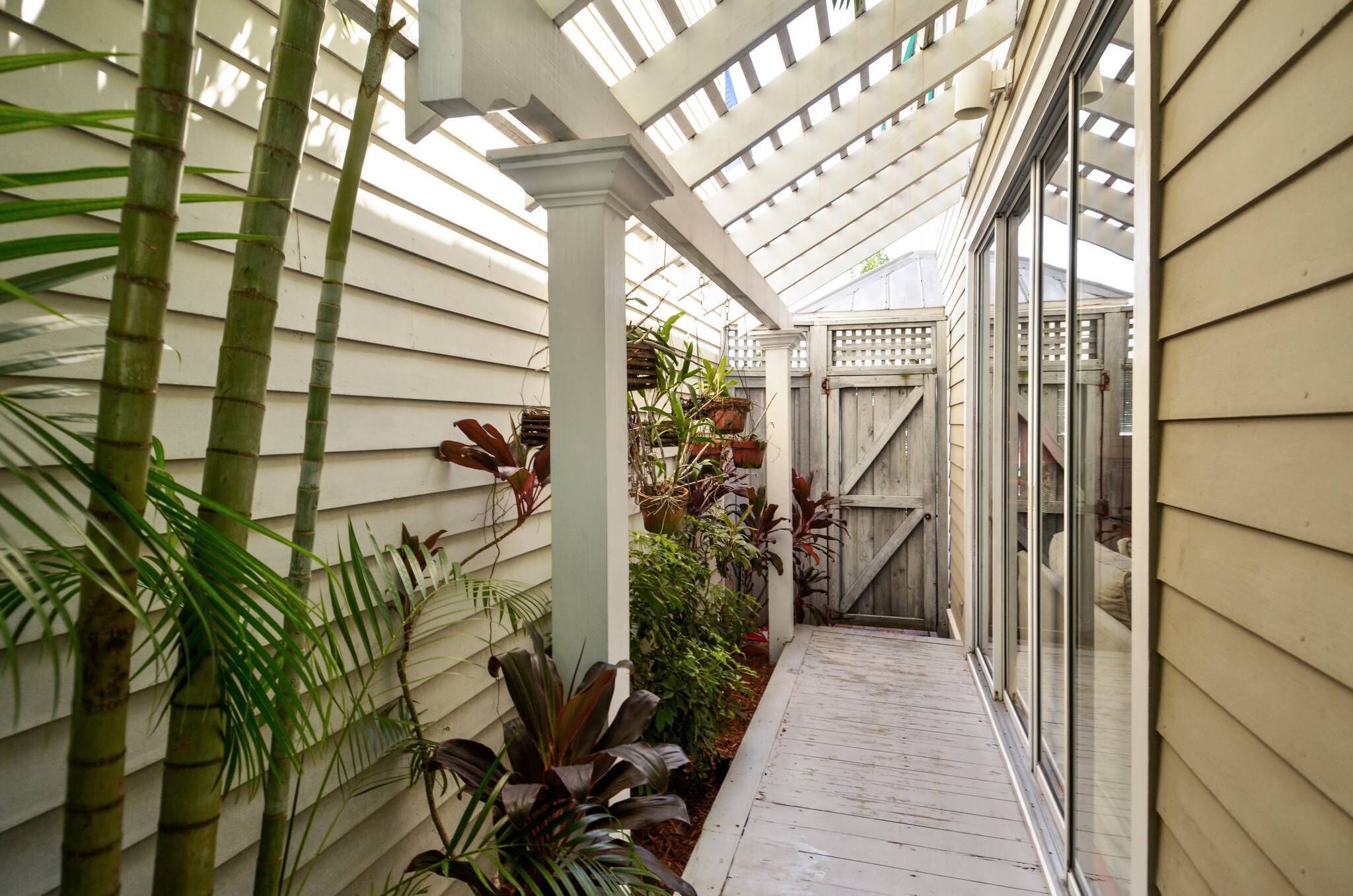 A covered walkway with bamboo plants, a wooden fence, and a glass door leading to a room.