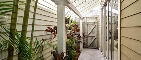 A covered walkway with bamboo plants, a wooden fence, and a glass door leading to a room.