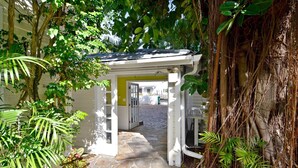 A stone pathway leading to a white gazebo with a yellow door, surrounded by lush greenery and a large tree with extensive roots. - Tranquility by AvantStay | Close to Duval St w/ BBQ & Shared Pool (Key West)