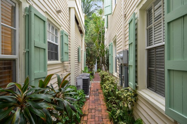 A narrow alleyway with buildings on either side, featuring green shutters and a brick pathway.